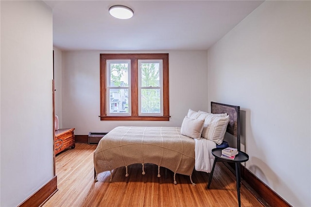 bedroom featuring light wood finished floors, baseboards, and a baseboard radiator