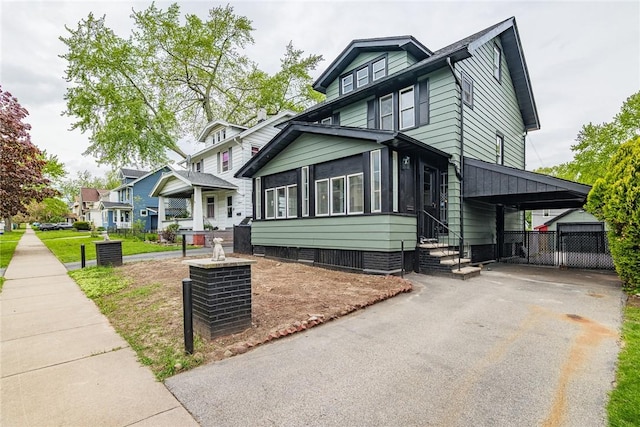 american foursquare style home featuring asphalt driveway, a sunroom, entry steps, a carport, and fence