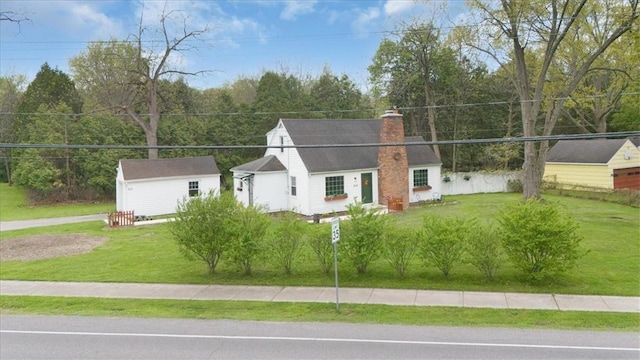 view of front of house featuring a chimney, a front yard, and an outbuilding