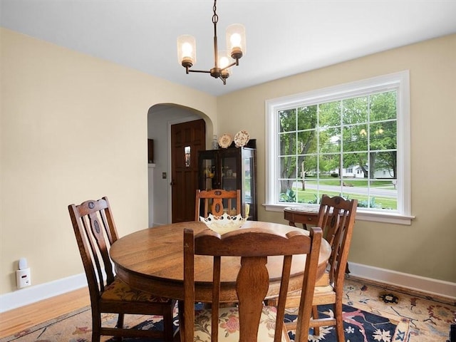 dining area featuring arched walkways, baseboards, a chandelier, and light wood-style flooring