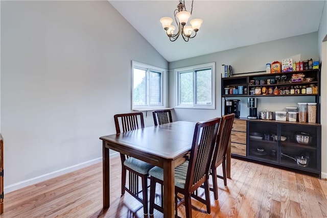 dining area featuring a chandelier, light wood finished floors, lofted ceiling, and baseboards