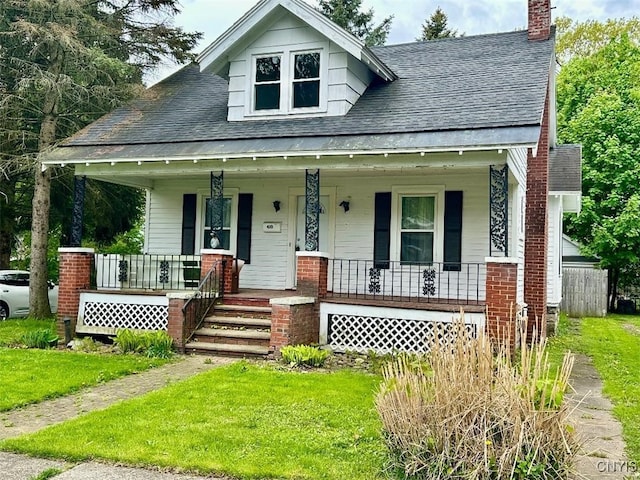 bungalow featuring a porch, roof with shingles, a chimney, and a front yard