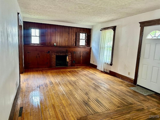 unfurnished living room featuring a brick fireplace, wood-type flooring, a textured ceiling, healthy amount of natural light, and baseboards
