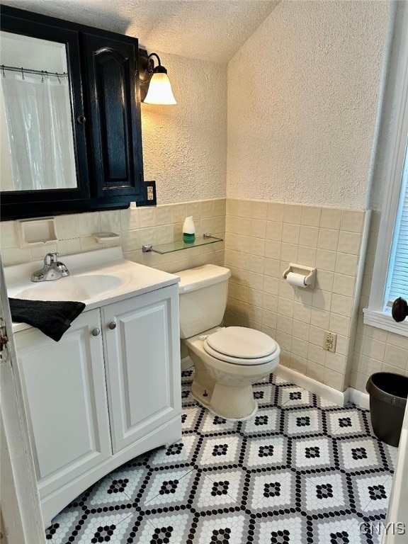 full bathroom with a textured wall, tile walls, toilet, vanity, and tile patterned floors