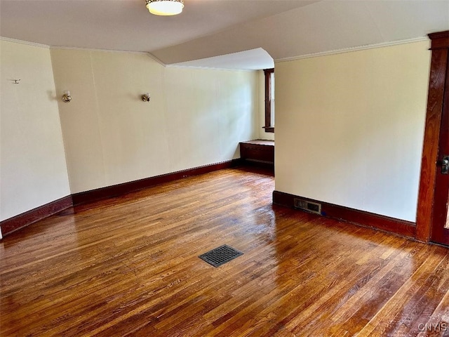 empty room featuring hardwood / wood-style flooring, ornamental molding, lofted ceiling, and baseboards