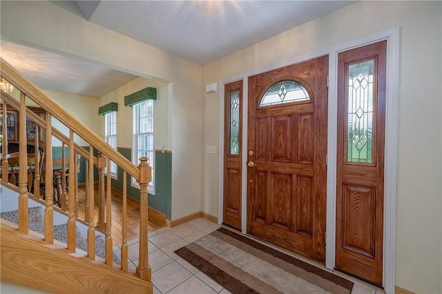entrance foyer with stairway, light tile patterned flooring, healthy amount of natural light, and baseboards