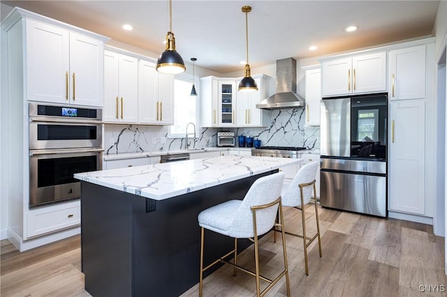 4490 Lauder Ln, Skaneateles, NY 13152 - kitchen with wall chimney exhaust hood, stainless steel appliances, a sink, light wood-style floors, and white cabinets