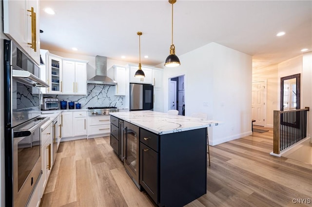 4490 Lauder Ln, Skaneateles, NY 13152 - kitchen with wall chimney range hood, stainless steel appliances, light wood-type flooring, backsplash, and a kitchen island