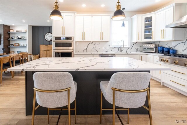 4490 Lauder Ln, Skaneateles, NY 13152 - kitchen with wall chimney range hood, appliances with stainless steel finishes, white cabinets, a kitchen bar, and recessed lighting