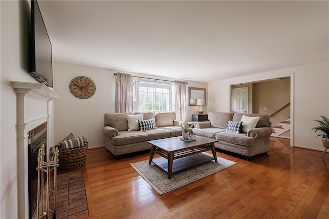 living area featuring wood-type flooring, a fireplace with flush hearth, stairs, and baseboards