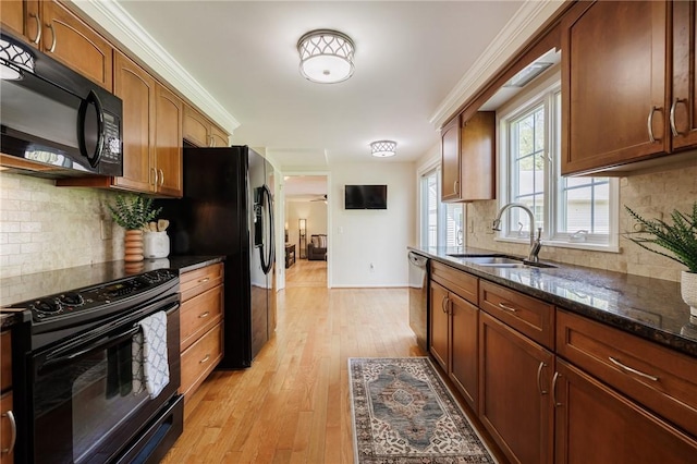 kitchen with black appliances, a sink, dark stone countertops, decorative backsplash, and light wood-style flooring