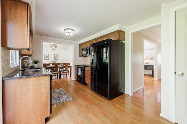 kitchen featuring black appliances, a sink, light wood-style floors, dark stone counters, and crown molding