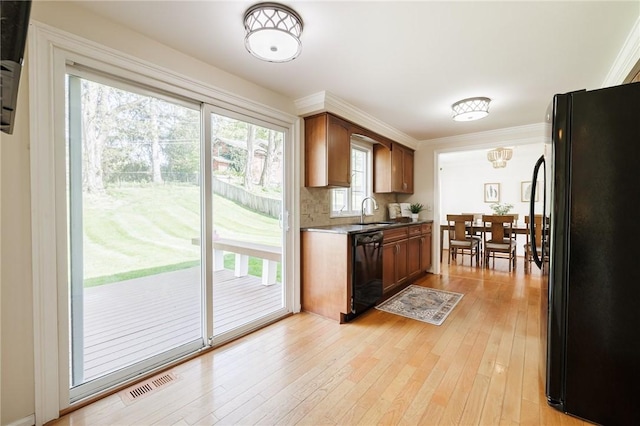 kitchen featuring black appliances, a sink, light wood-style flooring, crown molding, and tasteful backsplash