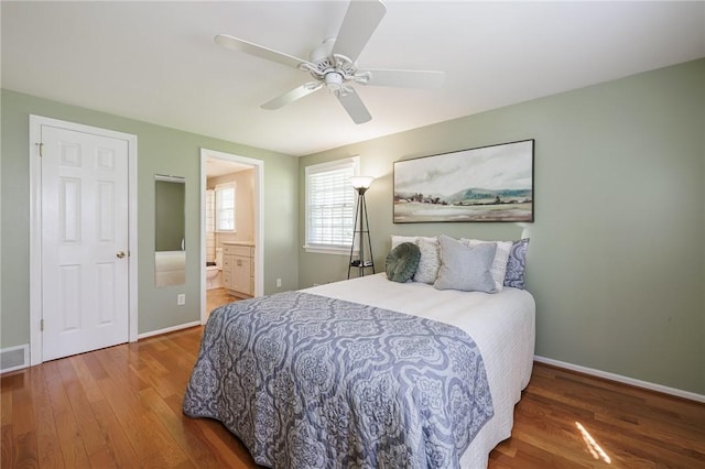 bedroom featuring wood finished floors, baseboards, ensuite bathroom, and a ceiling fan