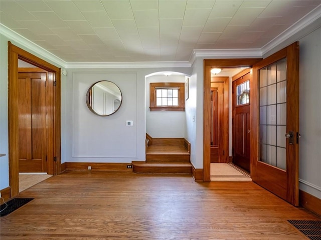 foyer with wood finished floors, baseboards, crown molding, and arched walkways