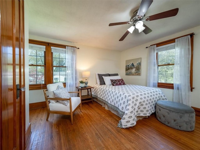 bedroom featuring wood finished floors, multiple windows, baseboards, and ceiling fan