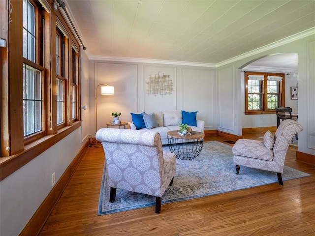 living room featuring ornamental molding, arched walkways, wood finished floors, baseboards, and a decorative wall