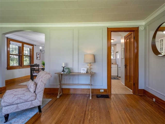 living area with crown molding, arched walkways, wood finished floors, and baseboards