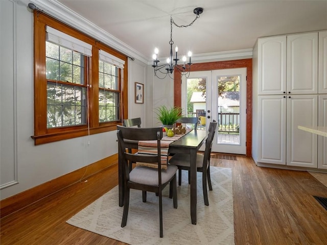 dining room with a chandelier, plenty of natural light, light wood finished floors, crown molding, and french doors
