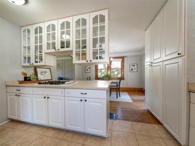 kitchen with white gas cooktop, light countertops, glass insert cabinets, light tile patterned flooring, and crown molding