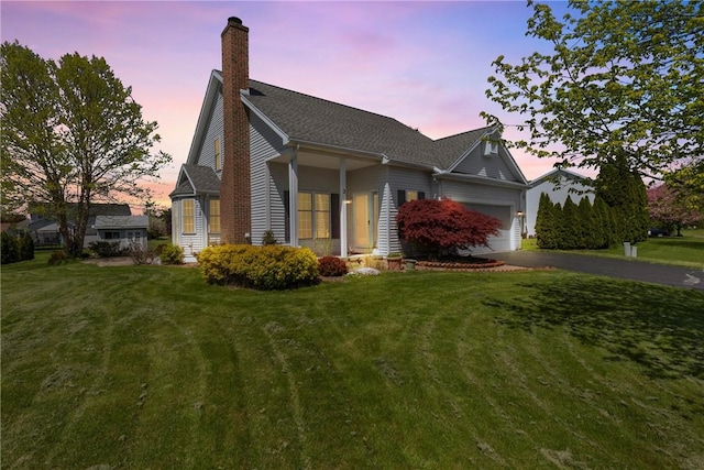 view of front facade with an attached garage, driveway, a front yard, and a chimney