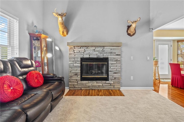 carpeted living area featuring a towering ceiling, a stone fireplace, wood finished floors, and baseboards