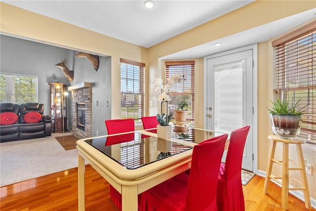 dining room with wood finished floors, a stone fireplace, and recessed lighting