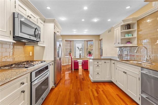 kitchen featuring stainless steel appliances, a sink, a peninsula, recessed lighting, and light wood-style flooring