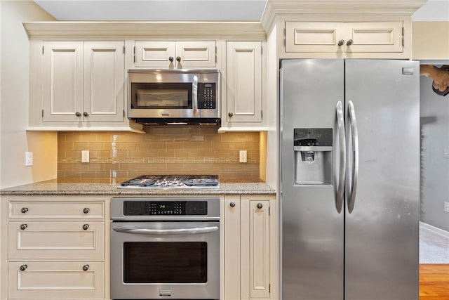 kitchen with stainless steel appliances, cream cabinets, and backsplash