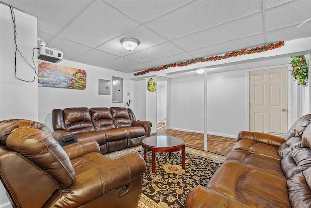 living room featuring a paneled ceiling, electric panel, and baseboards