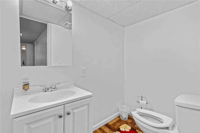 half bathroom featuring toilet, a drop ceiling, vanity, and baseboards