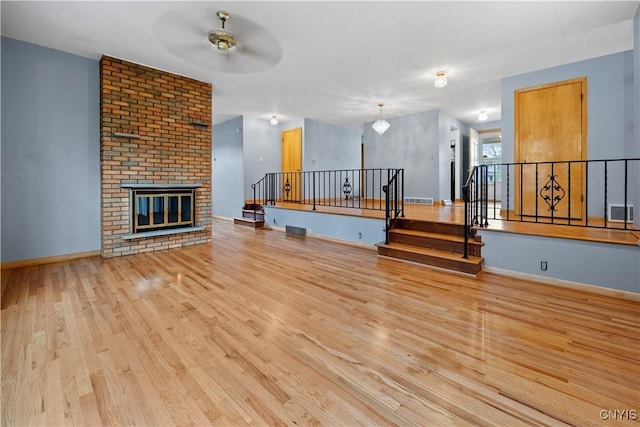7565 Audrey Dr, Clay, NY 13212 - unfurnished living room featuring wood finished floors, ceiling fan, baseboards, a brick fireplace, and stairs