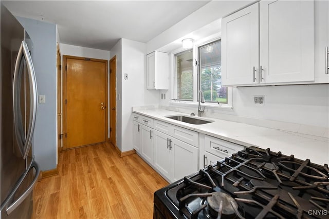 7565 Audrey Dr, Clay, NY 13212 - kitchen featuring freestanding refrigerator, a sink, black gas range, light wood-type flooring, and white cabinetry
