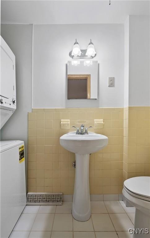 7565 Audrey Dr, Clay, NY 13212 - half bath featuring stacked washing machine and dryer, tile walls, toilet, tile patterned flooring, and a sink