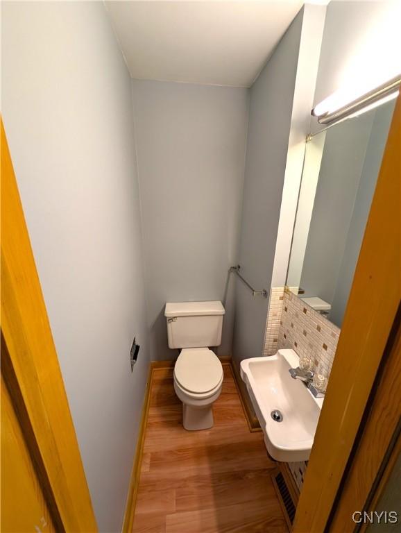 7565 Audrey Dr, Clay, NY 13212 - half bathroom with toilet, wood finished floors, baseboards, decorative backsplash, and a sink
