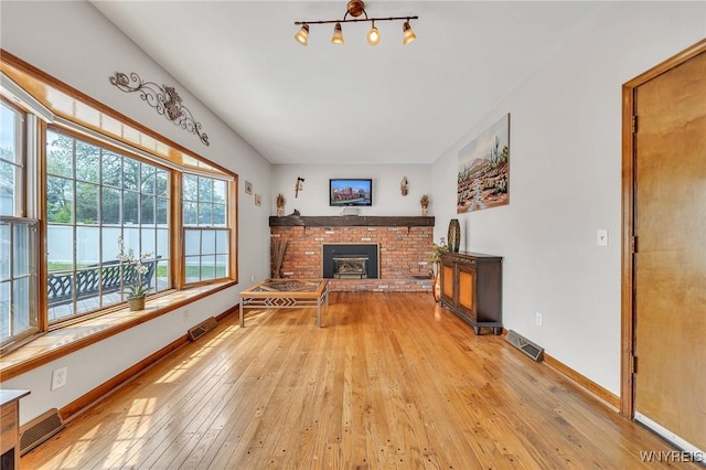 living area with a brick fireplace, light wood-style floors, and baseboards