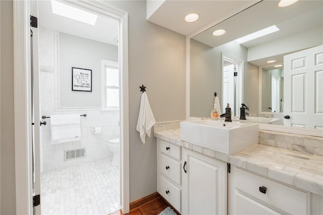 full bath featuring a skylight, toilet, vanity, tile walls, and recessed lighting