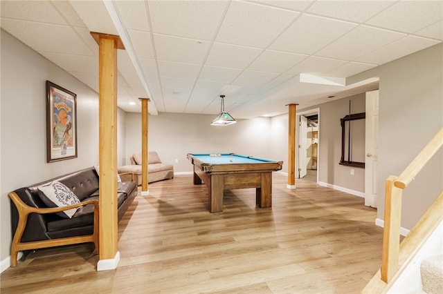 recreation room featuring a paneled ceiling, light wood-style flooring, and baseboards