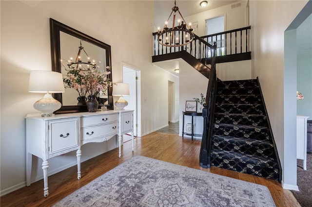 stairs featuring a chandelier, wood finished floors, a high ceiling, and baseboards