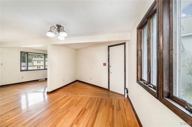 spare room featuring a chandelier, light wood-type flooring, and baseboards