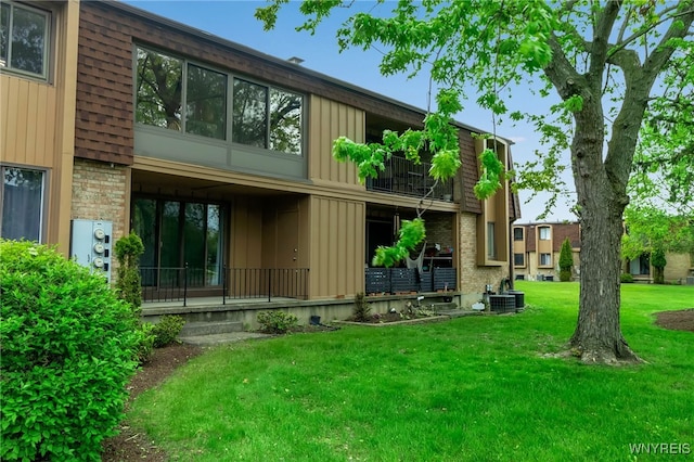 rear view of property featuring a balcony, a lawn, brick siding, and central AC