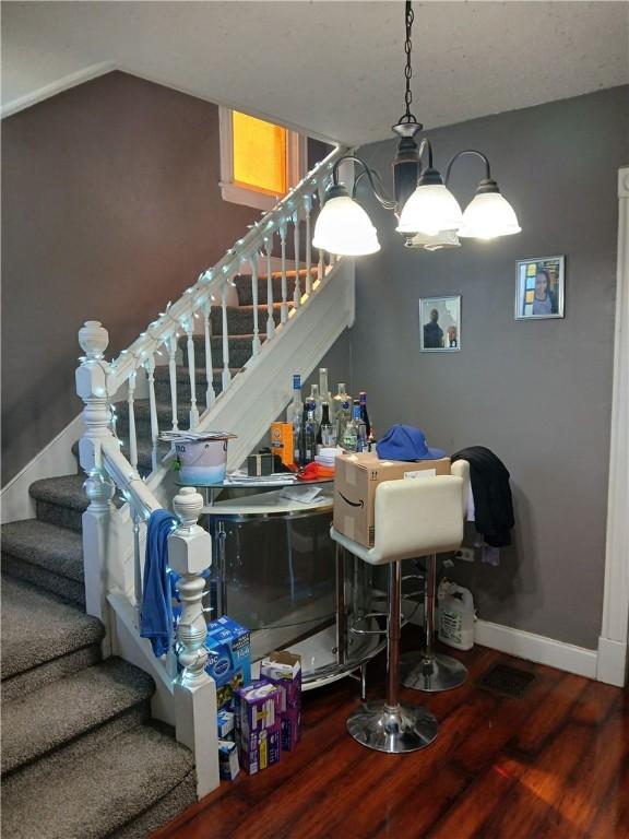 bar featuring stairs, wood finished floors, baseboards, a chandelier, and vaulted ceiling