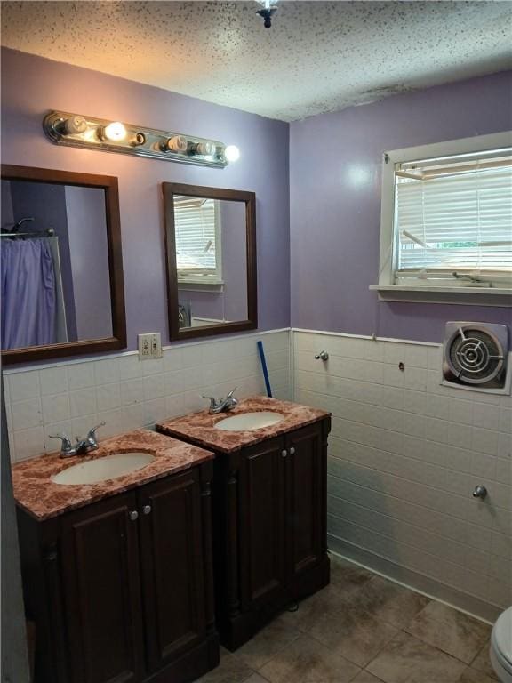 bathroom featuring tile walls, tile patterned flooring, two vanities, and a wainscoted wall
