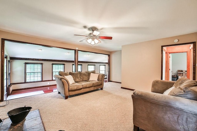 living area featuring ceiling fan, baseboards, and light colored carpet