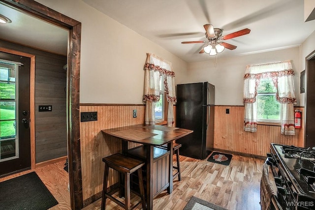kitchen featuring black appliances, a wainscoted wall, wood walls, light wood-style floors, and ceiling fan