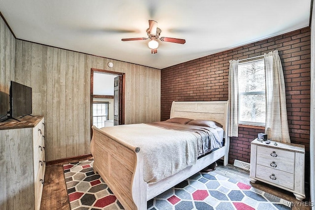 bedroom featuring multiple windows, brick wall, wood walls, and ceiling fan