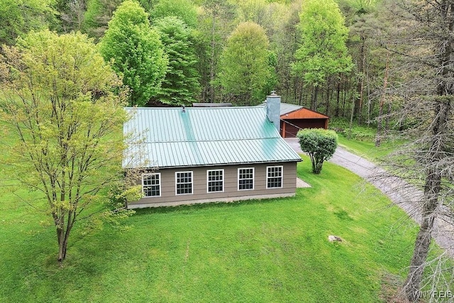 view of front of property featuring a front lawn, metal roof, a chimney, and a forest view