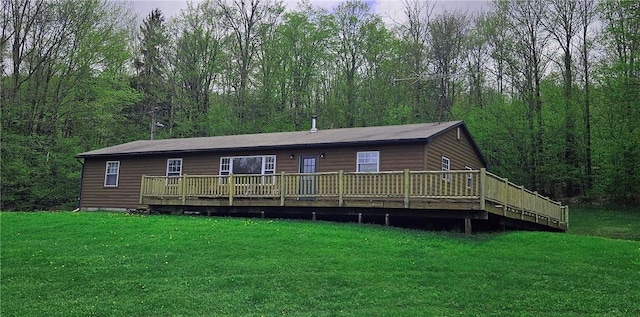 view of front facade with a deck, a front lawn, faux log siding, and a wooded view