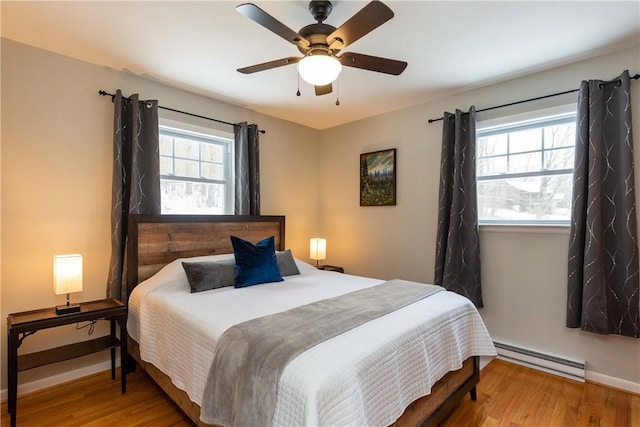 bedroom with baseboard heating, wood finished floors, baseboards, and a ceiling fan