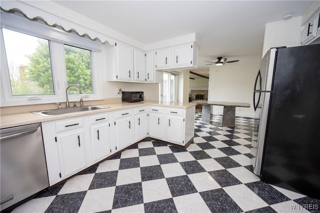 kitchen with stainless steel appliances, a sink, dark floors, ceiling fan, and light countertops
